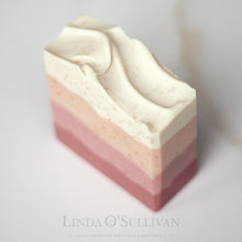 Load image into Gallery viewer, A handmade soap bar with horizontal layers of dusty rose, soft pink, and creamy off-white, with tiny gold speckles, photographed on a light marble surface. The brand name 'Linda O'Sullivan' is printed in a faint gray font at the bottom.
Handcrafted in the UK by Linda O'Sullivan.