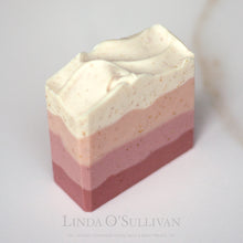 Load image into Gallery viewer, A handmade soap bar with horizontal layers of dusty rose, soft pink, and creamy off-white, with tiny gold speckles, photographed on a light marble surface. The brand name 'Linda O'Sullivan' is printed in a faint gray font at the bottom.
Handcrafted in the UK by Linda O'Sullivan.
