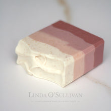 Load image into Gallery viewer, A handmade soap bar with horizontal layers of dusty rose, soft pink, and creamy off-white, with tiny gold speckles, photographed on a light marble surface. The brand name 'Linda O'Sullivan' is printed in a faint gray font at the bottom.
Handcrafted in the UK by Linda O'Sullivan.