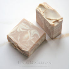 Load image into Gallery viewer, Two handmade soap bars with a swirled beige and cream pattern, displayed on a light marble surface. A single bar of handmade soap with a swirled pattern of light beige and off-white, photographed on a clean white background. Handmade in the UK by Linda O'Sullivan.